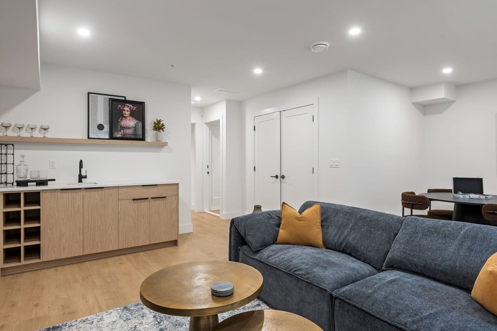 Archer at Latimer – Basement lounge with a navy sectional sofa, wet bar, and a dining table visible in the adjoining room.