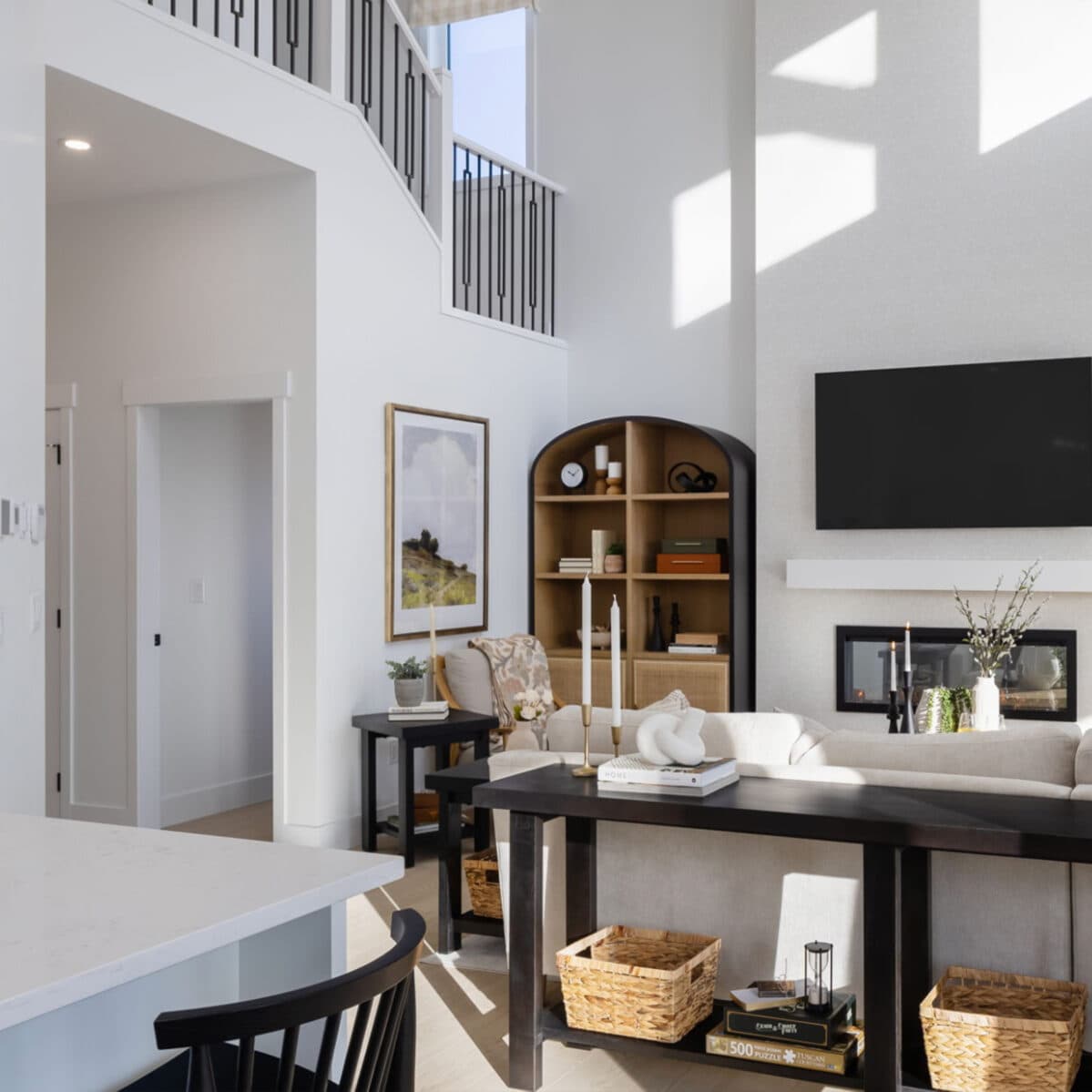 Station Grove – A two-story living room with a wall-mounted TV above a fireplace, a beige sectional sofa, and a black spiral staircase railing above.