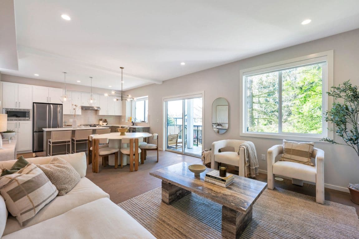 Fox and Aikins – Open-concept living, dining, and kitchen area with a round dining table, white sofa, and sliding doors to a balcony.