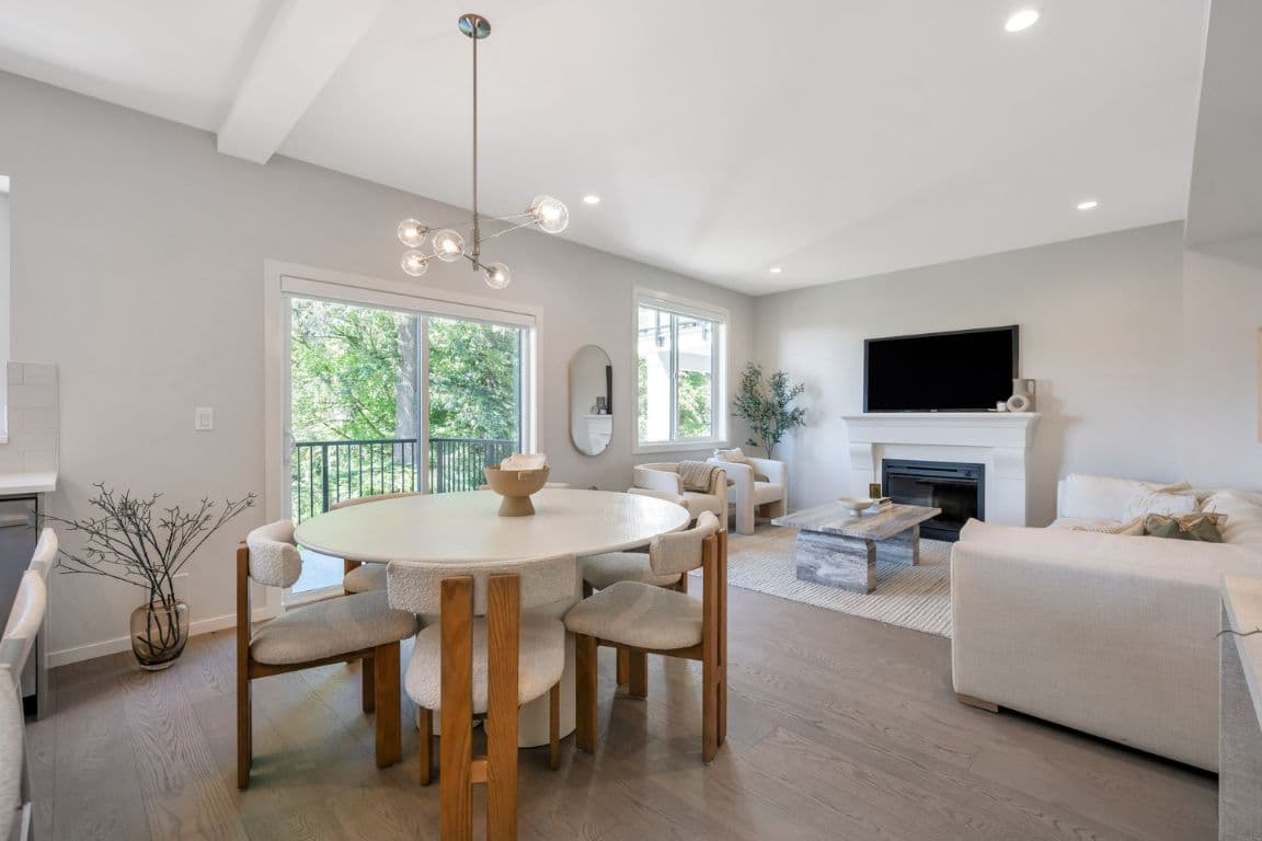 Fox and Aikins – Open-concept dining and living area with a round table, wood chairs, a fireplace with wall-mounted TV, and sliding doors to a balcony.