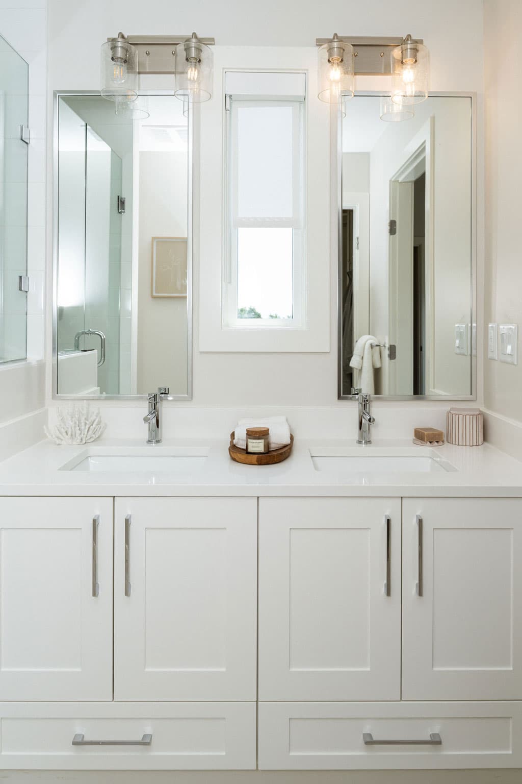 Fox and Aikins – Bathroom double sink vanity with framed mirrors, sconce lighting, chrome fixtures, and a window between the sinks.