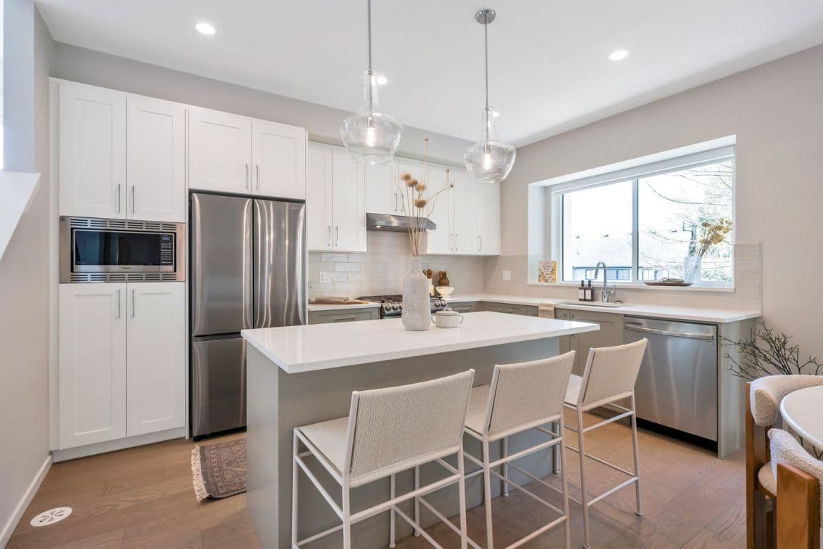Fox and Aikins – Kitchen with white cabinetry, stainless appliances, and a large island with pendant lighting, opening onto a bright window.