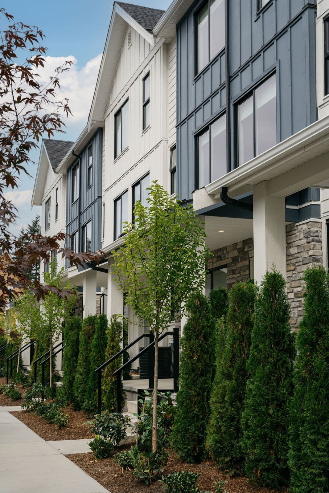 Fox and Aikins – Angled daytime view of a row of townhomes with white and dark blue-gray board-and-batten siding, stone accents, and covered front porches.