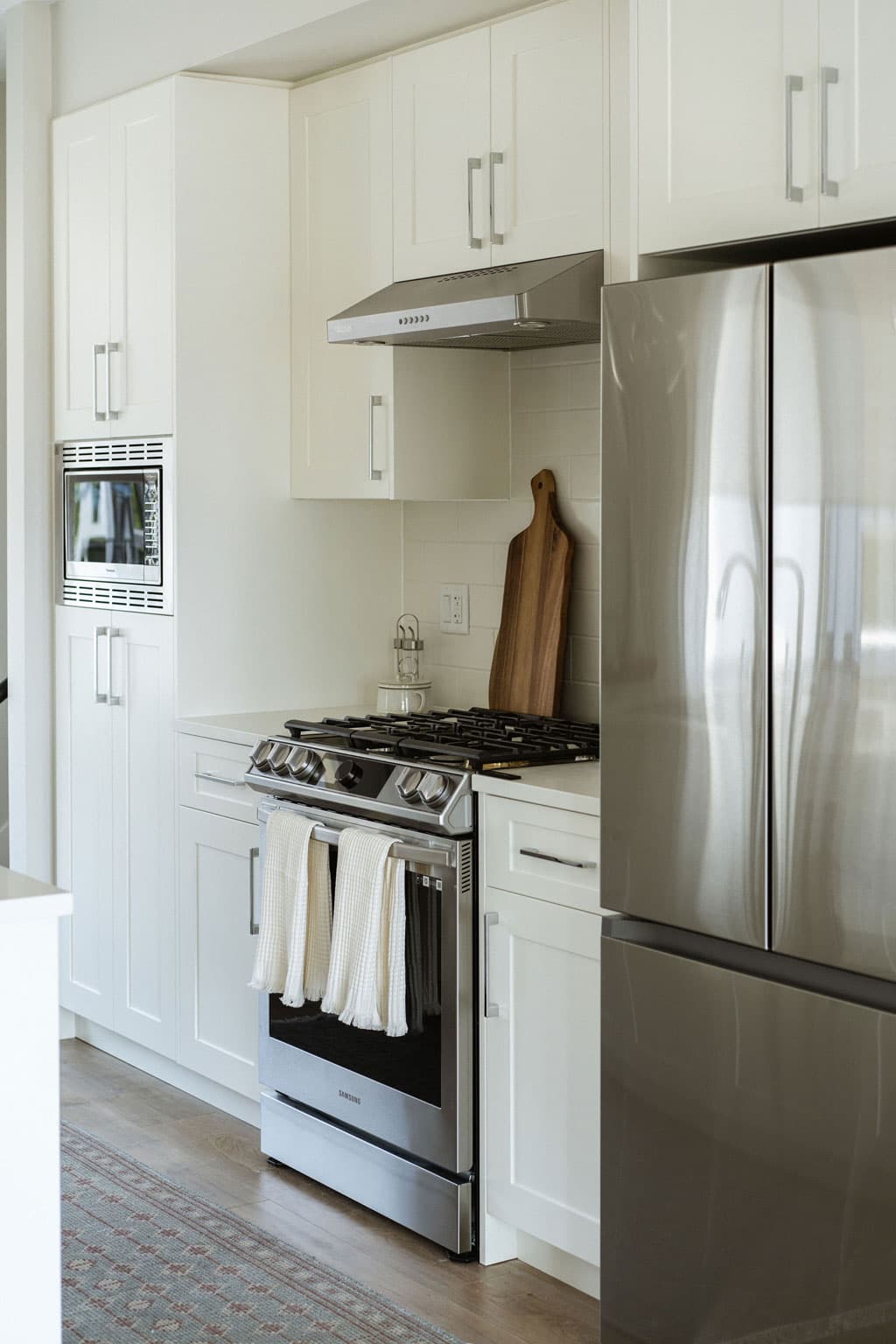 Fox and Aikins – Kitchen corner with white cabinetry, stainless steel range and built-in microwave, and a stainless refrigerator.