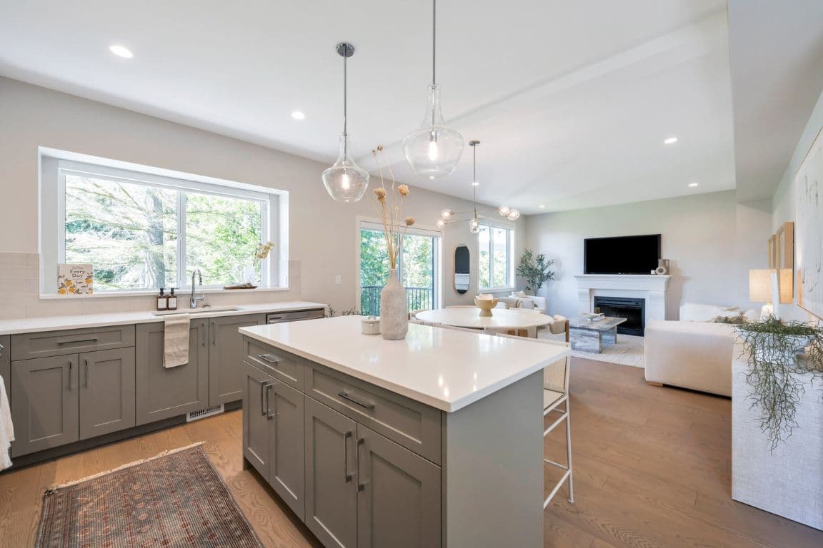 Fox and Aikins – Kitchen with grey cabinetry and a large island, opening into a living room with a fireplace and wall-mounted TV.