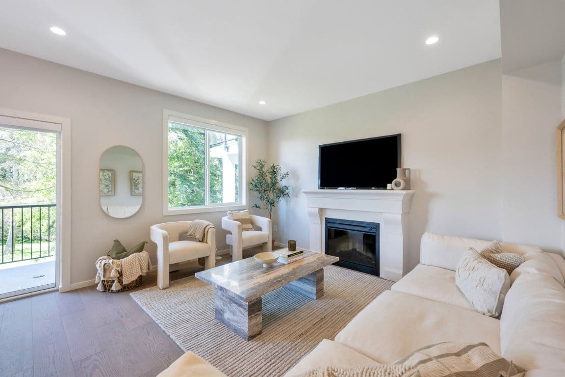 Fox and Aikins – Living room with a wall-mounted TV above a white mantel fireplace, cream sofa, armchairs, and sliding doors to a balcony.
