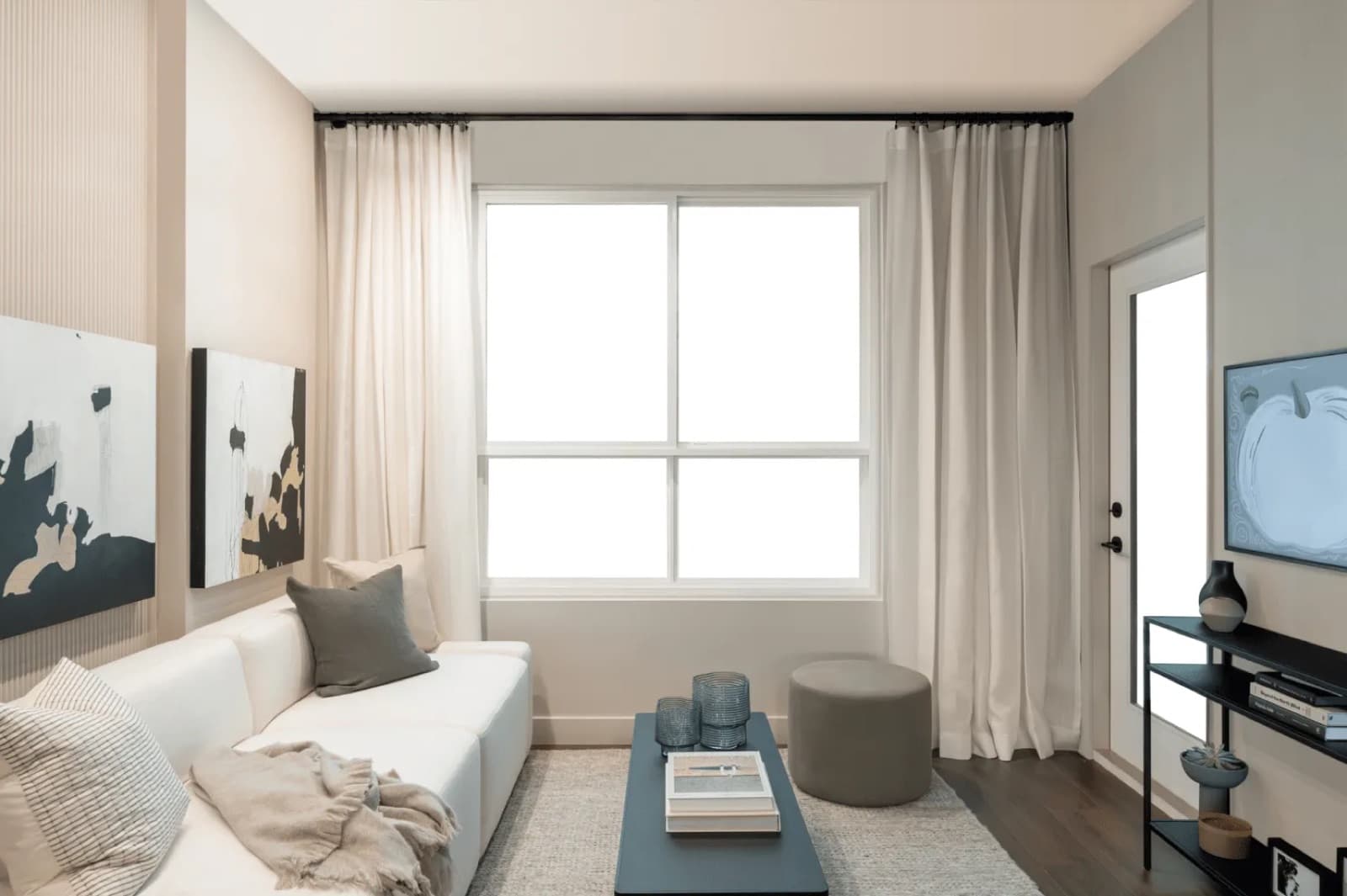 Rowan – A compact living room with a white sofa, throw blanket, dark coffee table, and wall-mounted TV near a glass door.