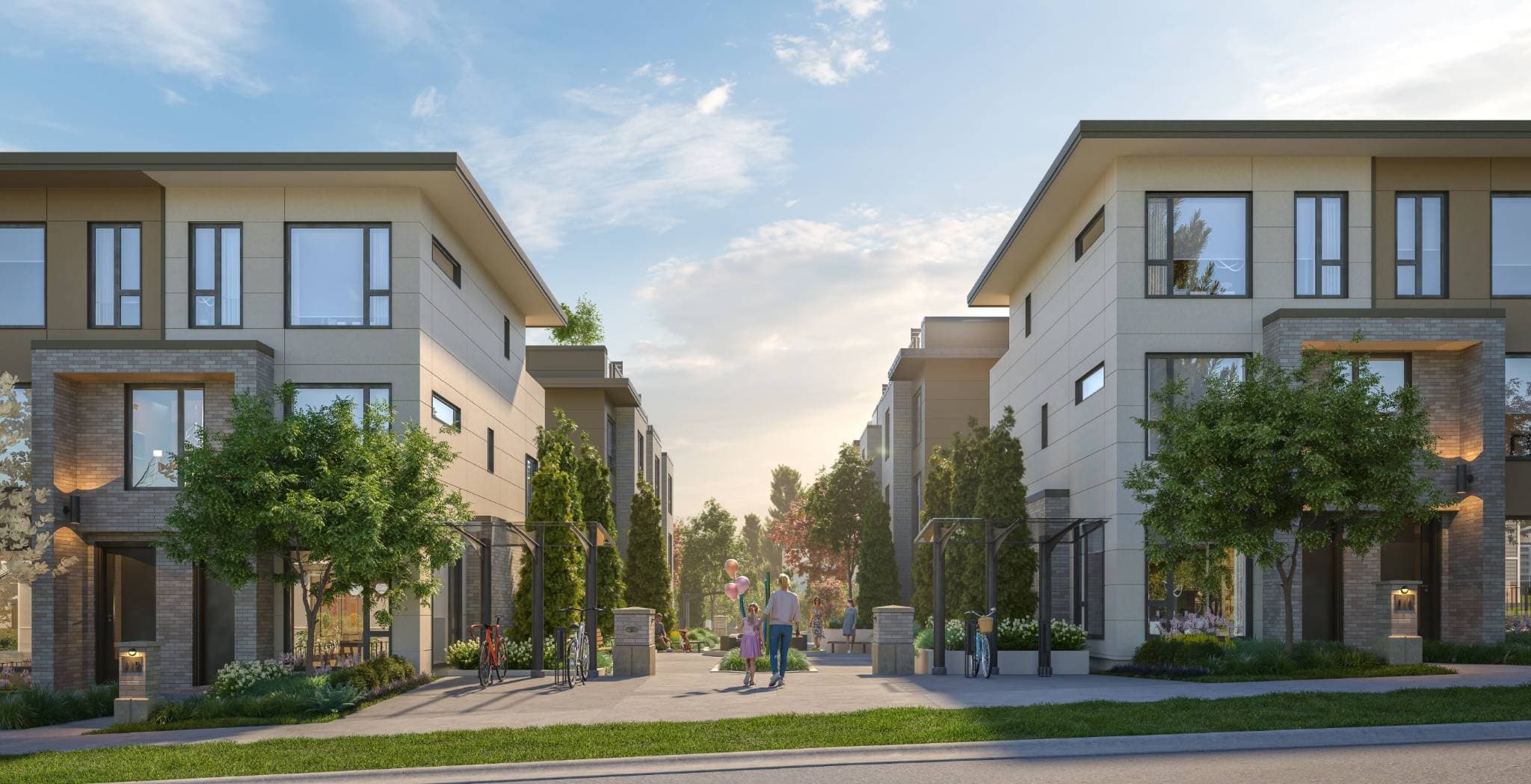 Harriswood – Street-level view of modern townhome buildings with a landscaped walkway between them where a family walks with balloons.