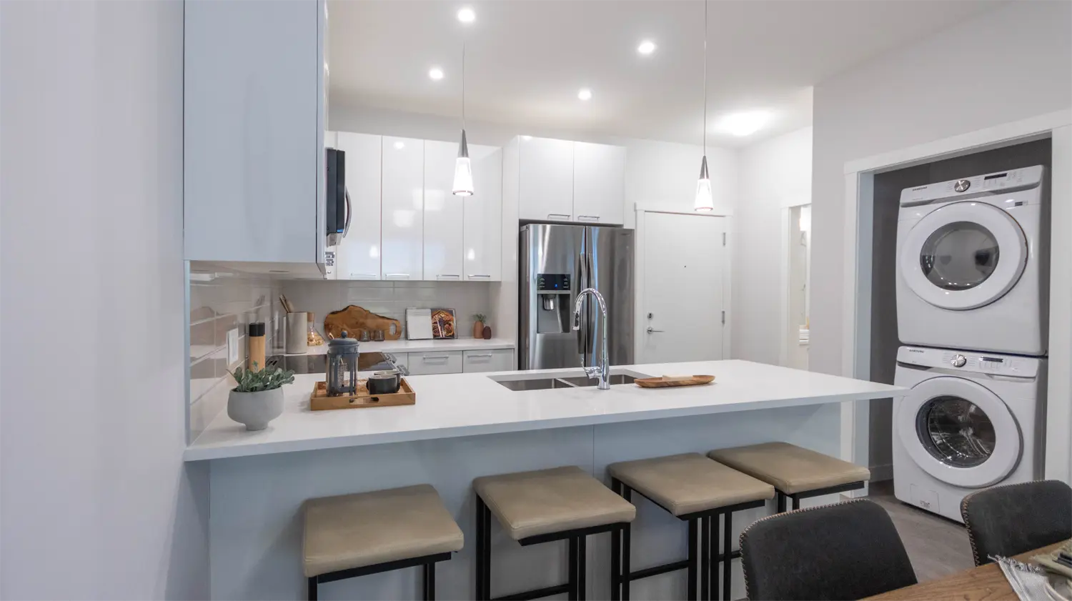 Montgomery – A kitchen with white cabinets and a stacked washer/dryer visible in an adjacent closet, with bar stool seating at the counter.