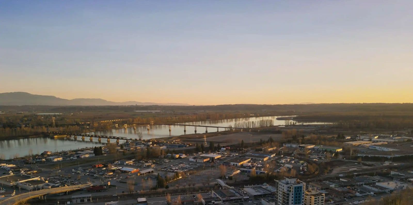 Montgomery – A drone photo at sunset showing a river, a rail bridge, and the surrounding town with mountains in the distance.