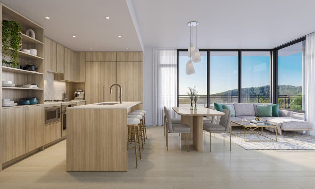 Alina – Open-concept kitchen with wood cabinetry, an island with gold-legged barstools, and a dining/living area with a grey sectional sofa in front of floor-to-ceiling windows showing a forested view.