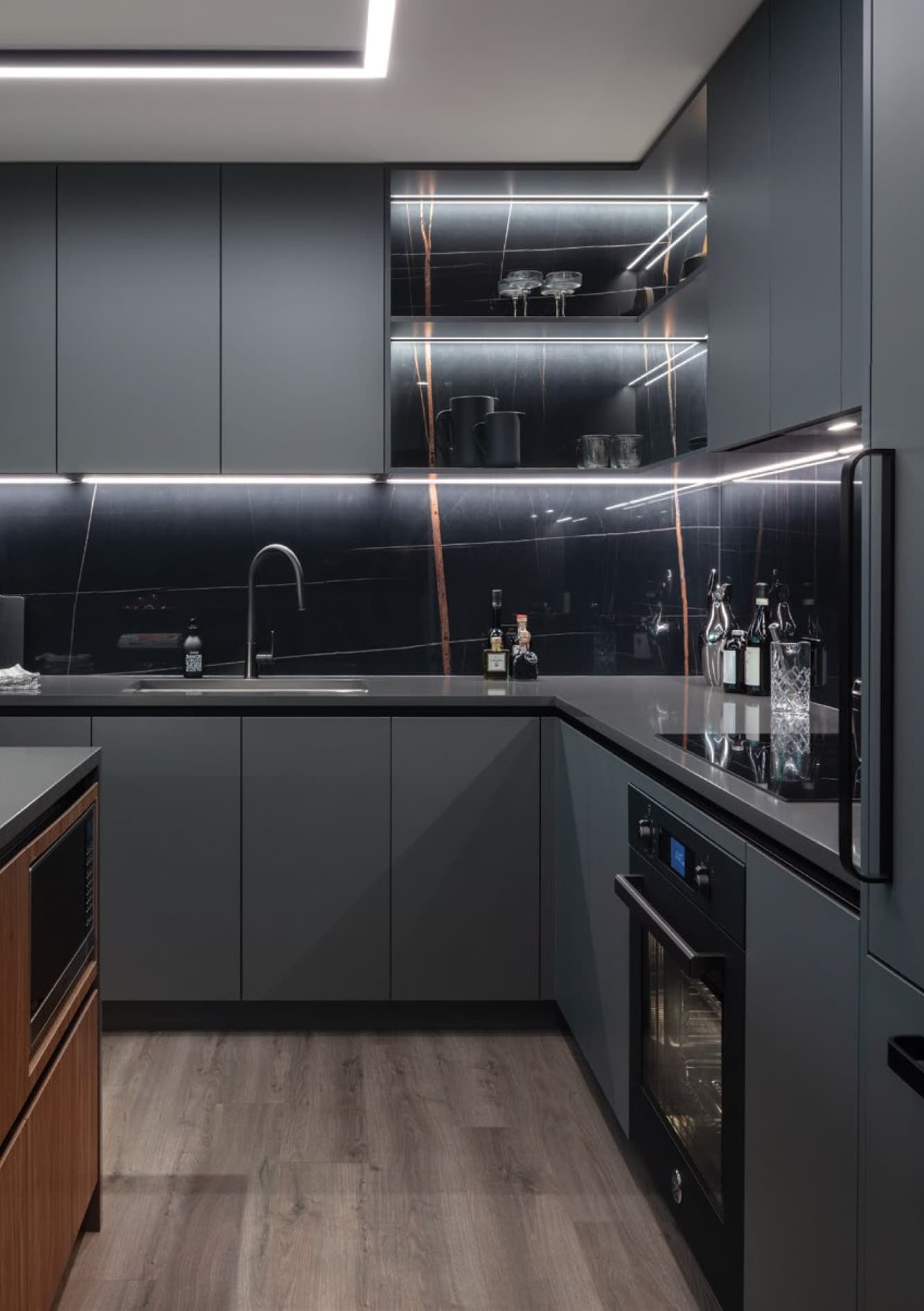 Bassano – Dark grey kitchen with black veined-marble backsplash, open shelving with glassware, built-in wine rack, and wood-front kitchen island.