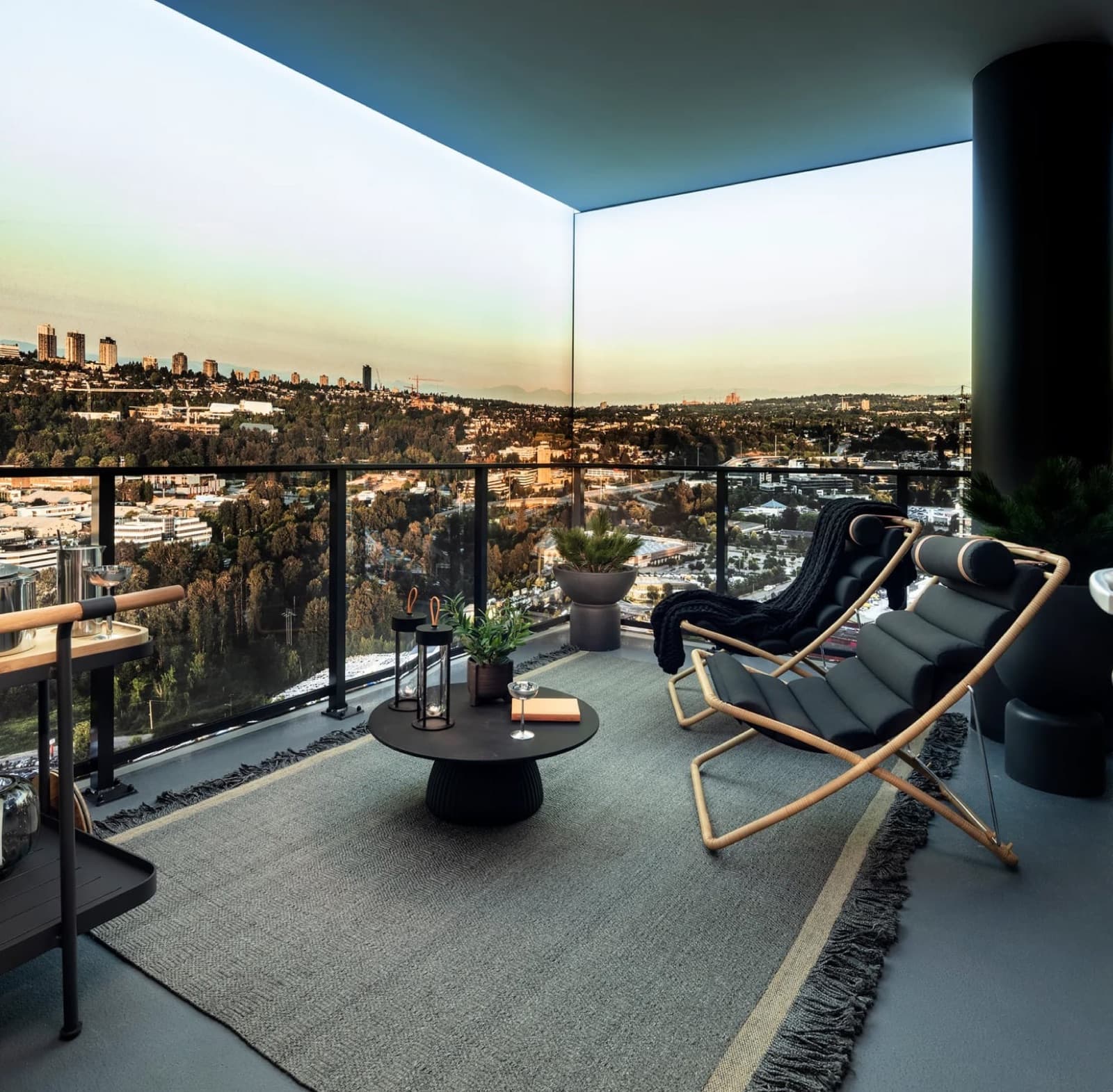 Bassano – Rooftop terrace lounge with lounge chairs, a round coffee table, potted plants, and a bar cart, overlooking a city skyline at dusk.