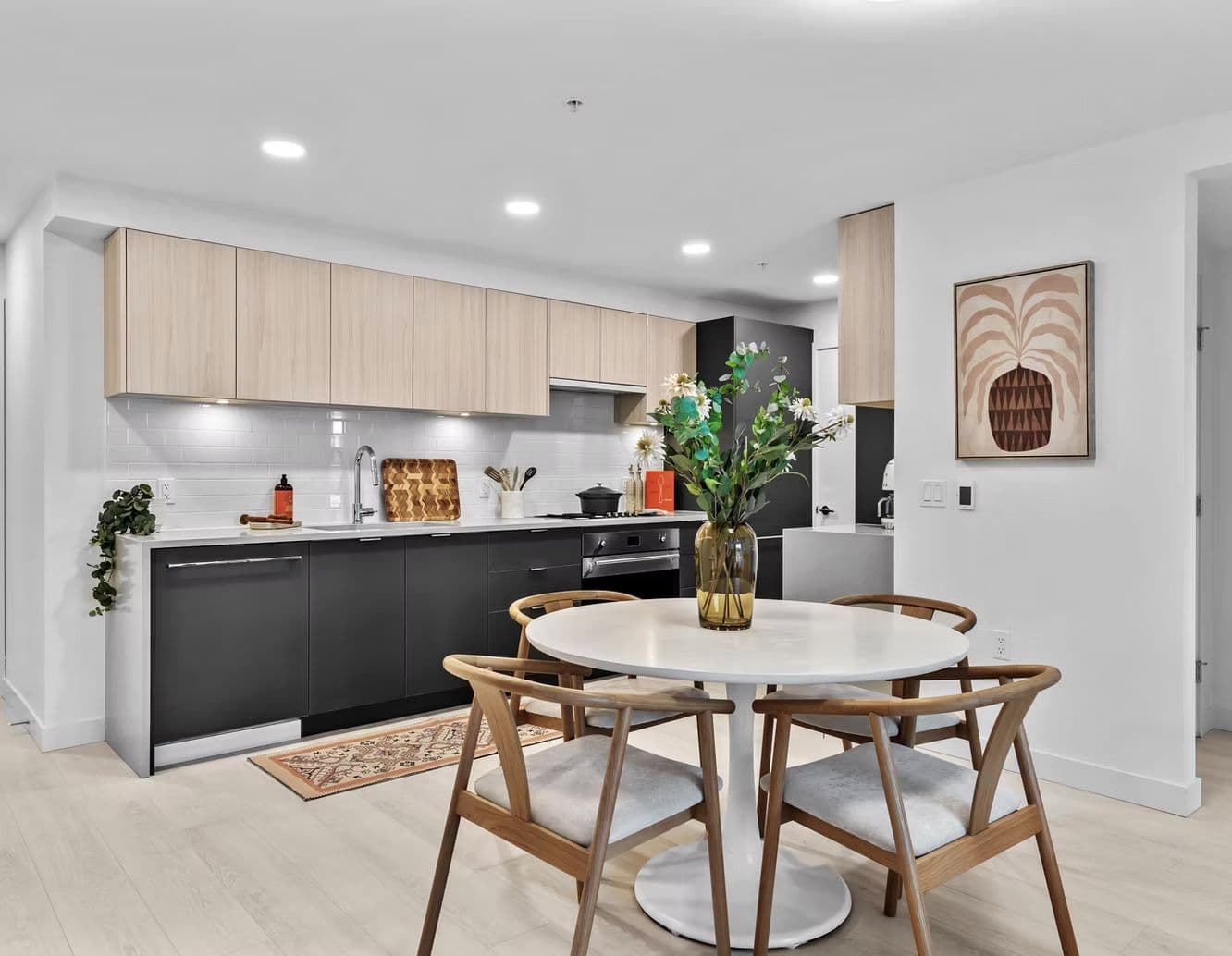 The Grant – Kitchen and dining area with light wood cabinets, dark lower cabinets, round dining table, and wood chairs.