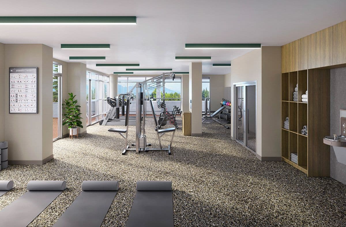 Walker House – A bright, modern fitness center with speckled gym flooring features various exercise equipment, including treadmills, stationery bikes, a multi-gym machine, and yoga mats laid out in the foreground. Large floor-to-ceiling windows offer natural light and views of treetops and mountains under a clear sky.