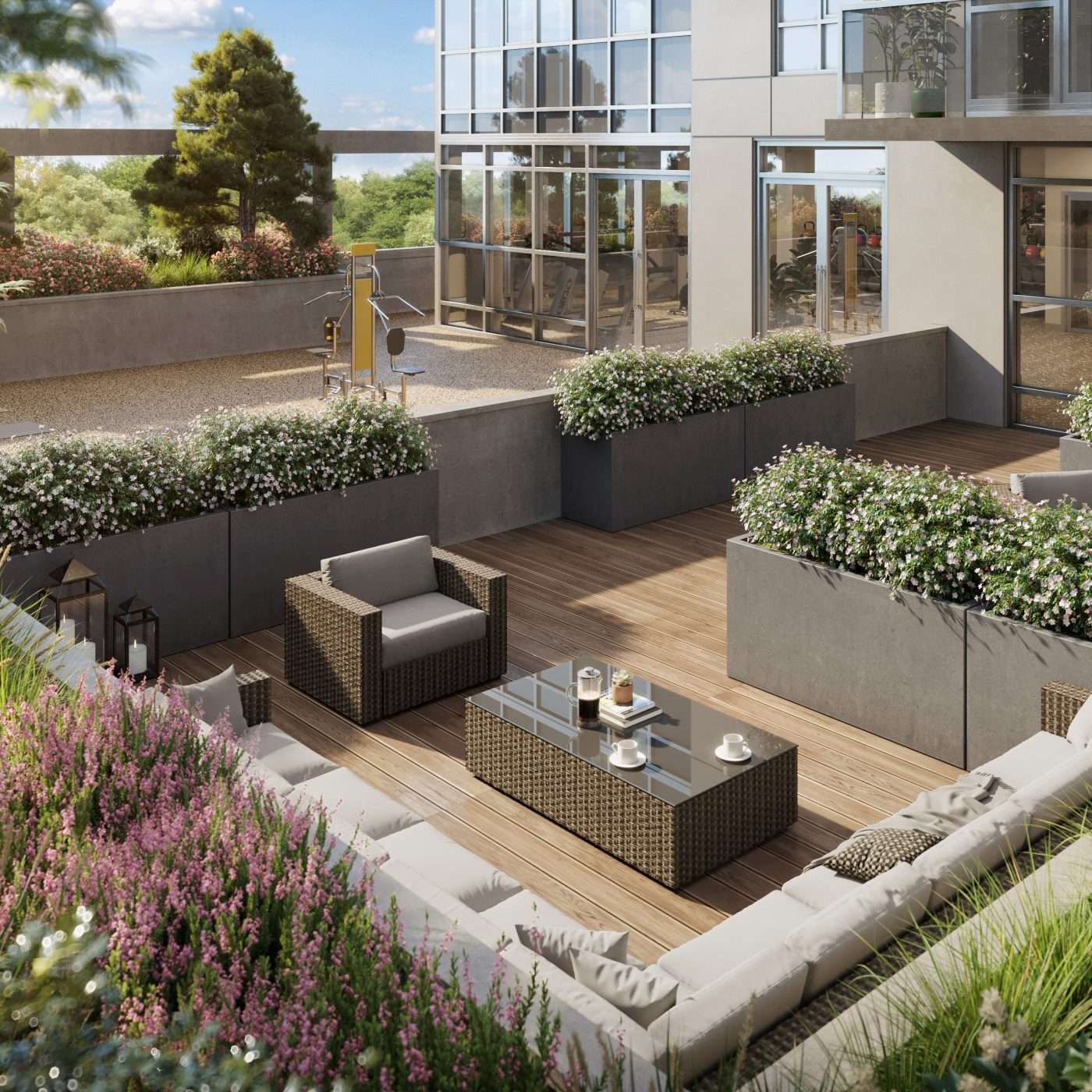 Walker House – An outdoor rooftop terrace feature plush L-shaped lounge seating, a wicker coffee table with coffee cups, and a single armchair set on wood decking. Concrete planters with flowering plants line the lounge space, while an adjacent gravel courtyard area contains outdoor exercise equipment in front of the building's glass windows.