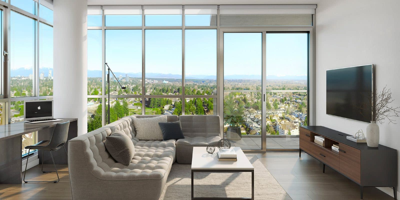 Walker House – A modern living room features a low-profile grey tufted sectional sofa, a white coffee table, and a wall-mounted TV above a dark wood media console. Floor-to-ceiling windows and sliding glass doors open to a balcony, offering bright daylight views of a leafy suburb extending toward distant mountains.