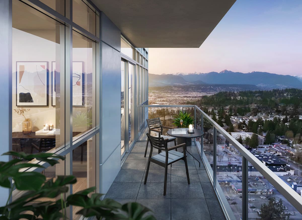Walker House – A high-rise balcony furnished with a small bistro table and two chairs overlooks a sprawling city and distant mountain range during a soft dusk light. Glass railings offer an unobstructed panoramic view, while floor-to-ceiling windows reflect the warm glow from the adjacent interior living space.