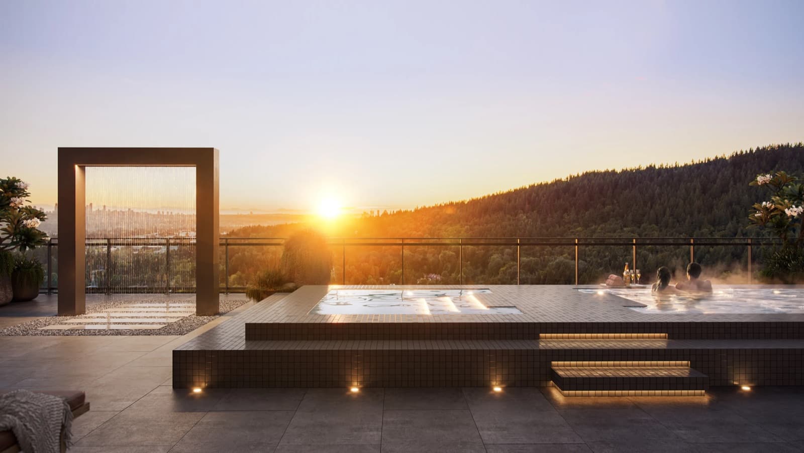 Kora – Rooftop hot tub and water feature at sunset with a couple relaxing in the water and forested mountains behind.