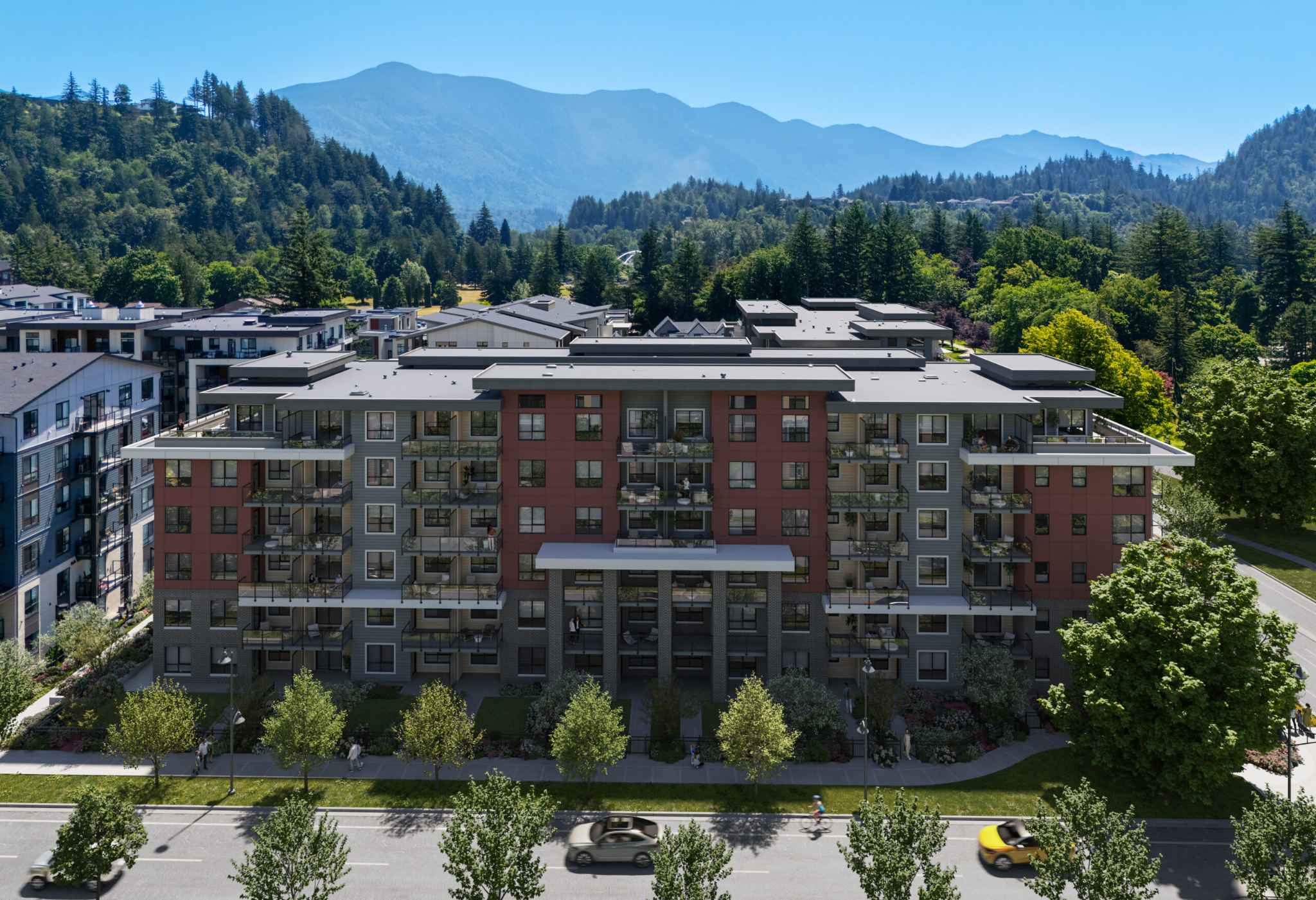 Queens Residences – An elevated shot showcases a modern six-story residential building featuring brick accents, red siding, and private balconies along a tree-lined street. Lush green forests and majestic blue mountain peaks rise in the clear daytime backdrop.