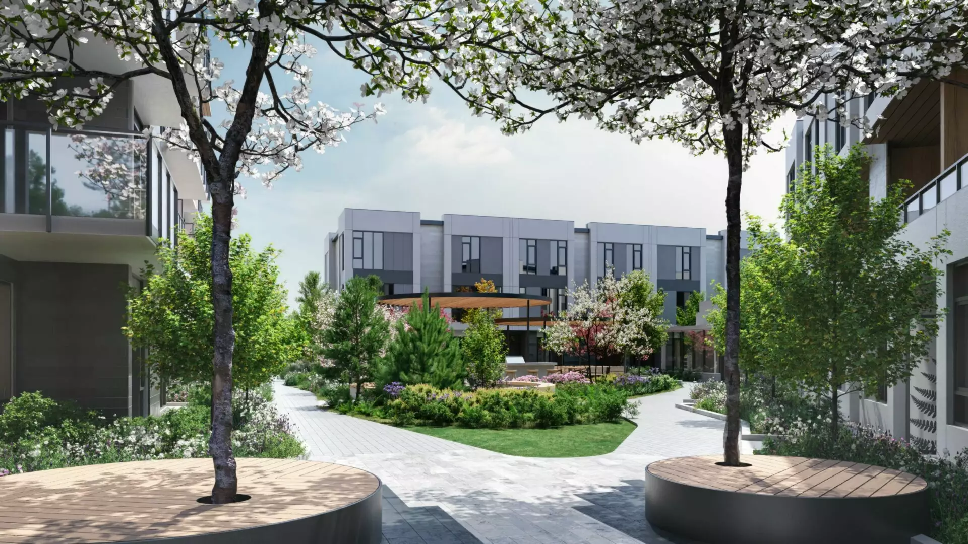 Edge Way at leləm̓ – A landscaped outdoor residential courtyard framed by blossoming trees and circular wood bench planters. Paved pathways wind past lush garden beds, a lawn area, and a covered pergola pavilion set against the backdrop of modern multi-story residential buildings under bright daylight.