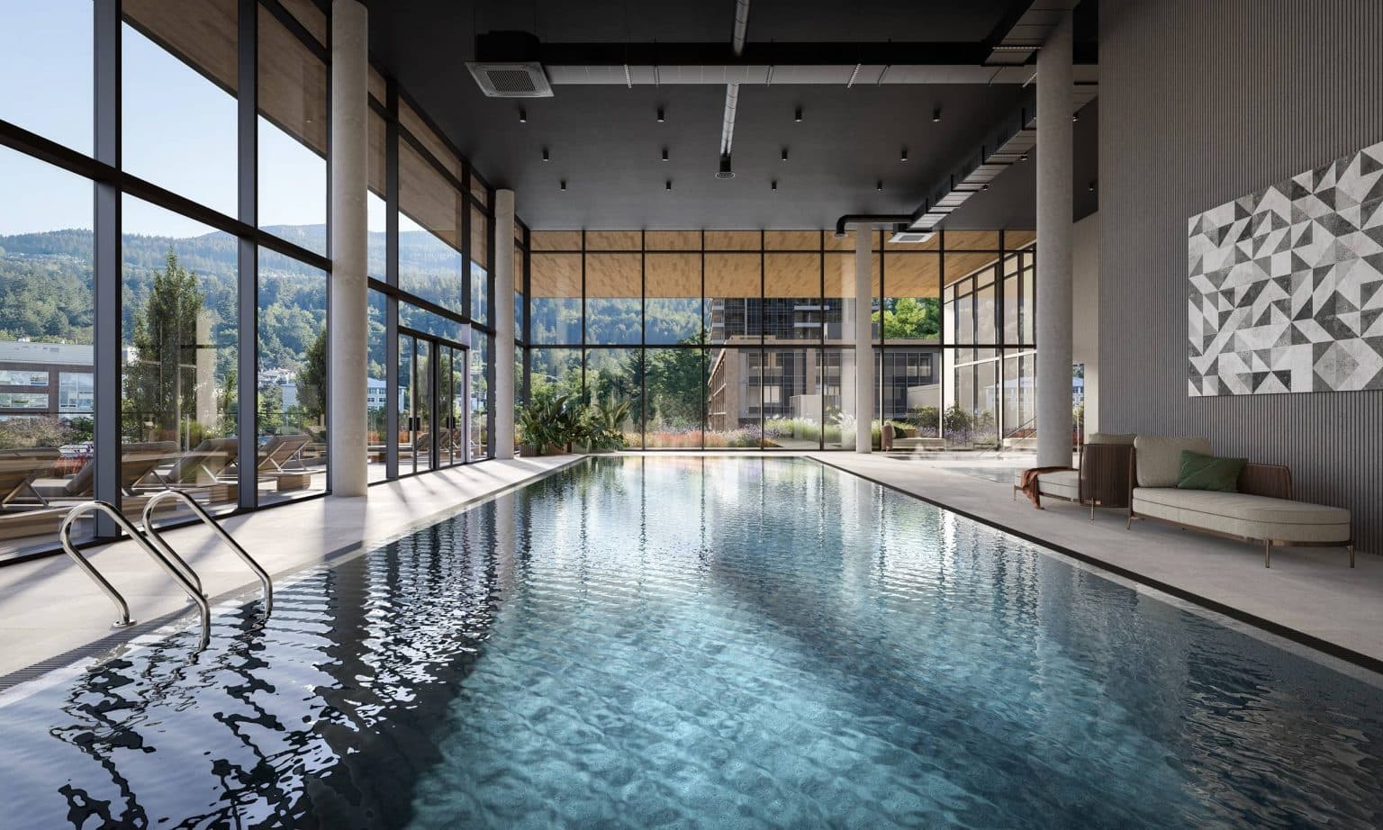 Inlet District – A luxurious indoor lap pool features clear rippling water surrounded by light stone tiling and contemporary lounge seating. Floor-to-ceiling glass walls flood the high-ceilinged space with daylight, offering views of an outdoor terrace, nearby modern buildings, and forested hills in the distance.