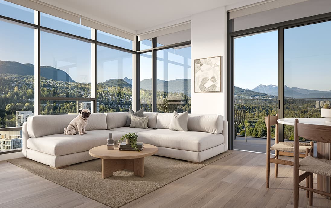 Inlet District – A sunlit, modern corner living room features light hardwood floors, a low-profile cream sectional sofa with a small pug sitting on it, and a round wooden coffee table. Expansive floor-to-ceiling windows and a sliding glass balcony door showcase panoramic daytime views of lush forested hills and distant mountains under a clear blue sky.