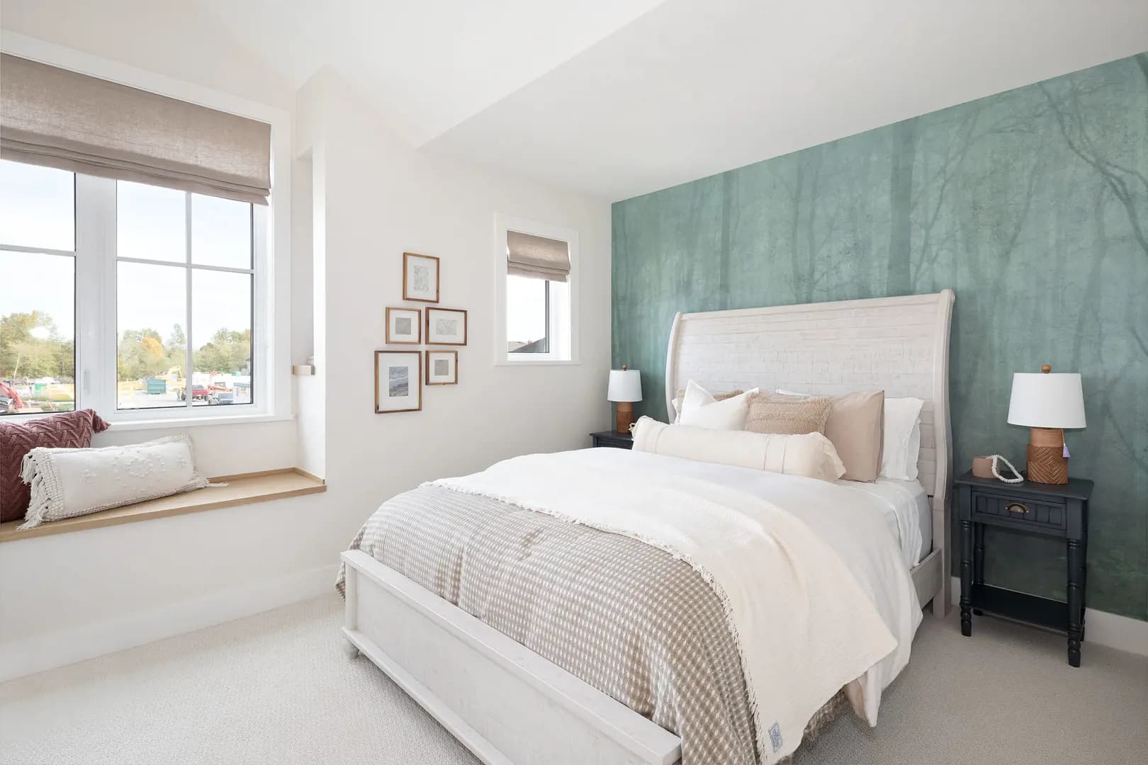Ridgemont – Bedroom with a teal forest-pattern accent wall, white upholstered bed, patterned bedding, a window seat with cushions, and small framed art.
