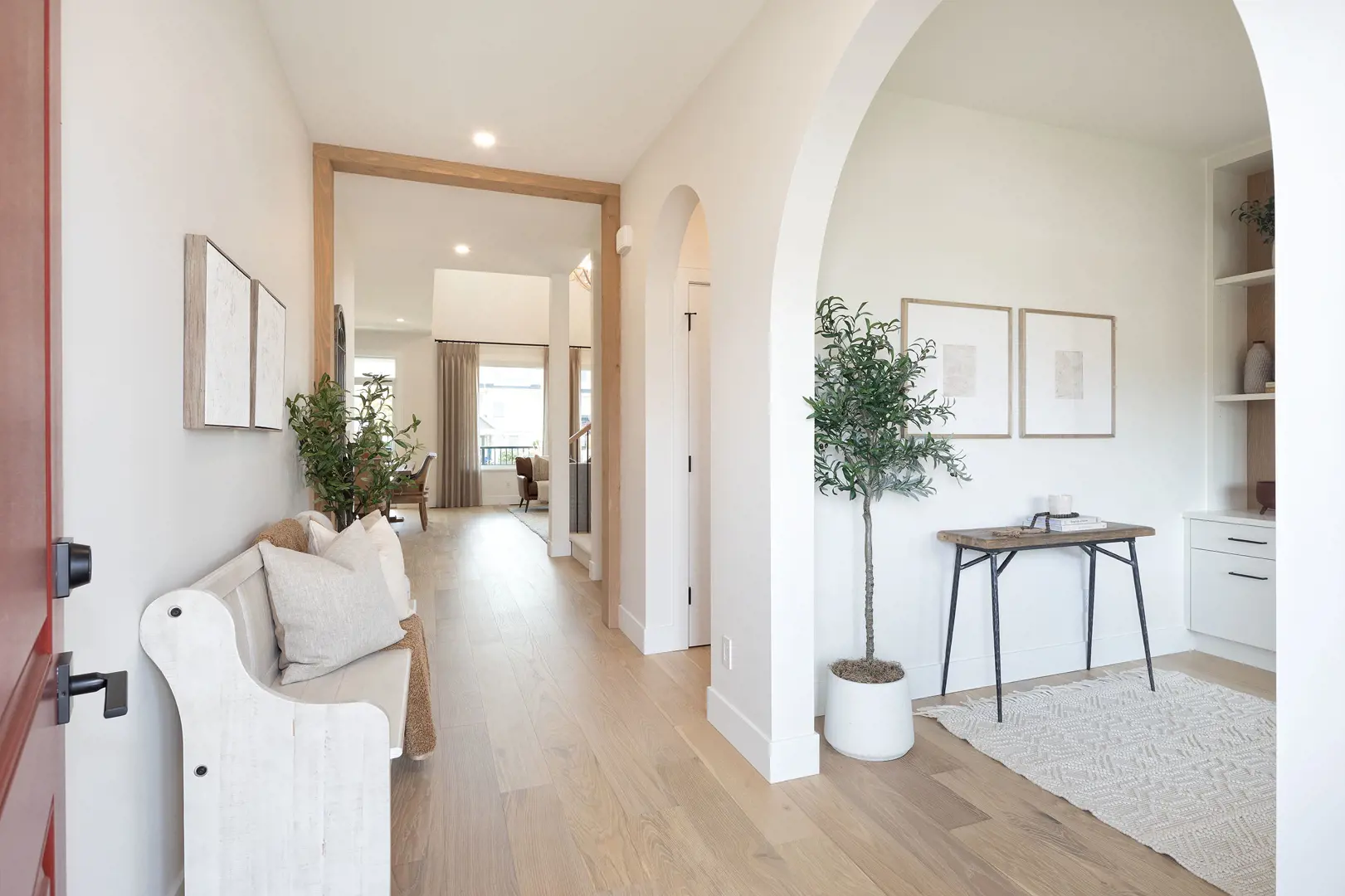 Ridgemont – Bright entryway hall with arched openings, wood flooring, a white bench, potted olive trees, framed art and a console table.