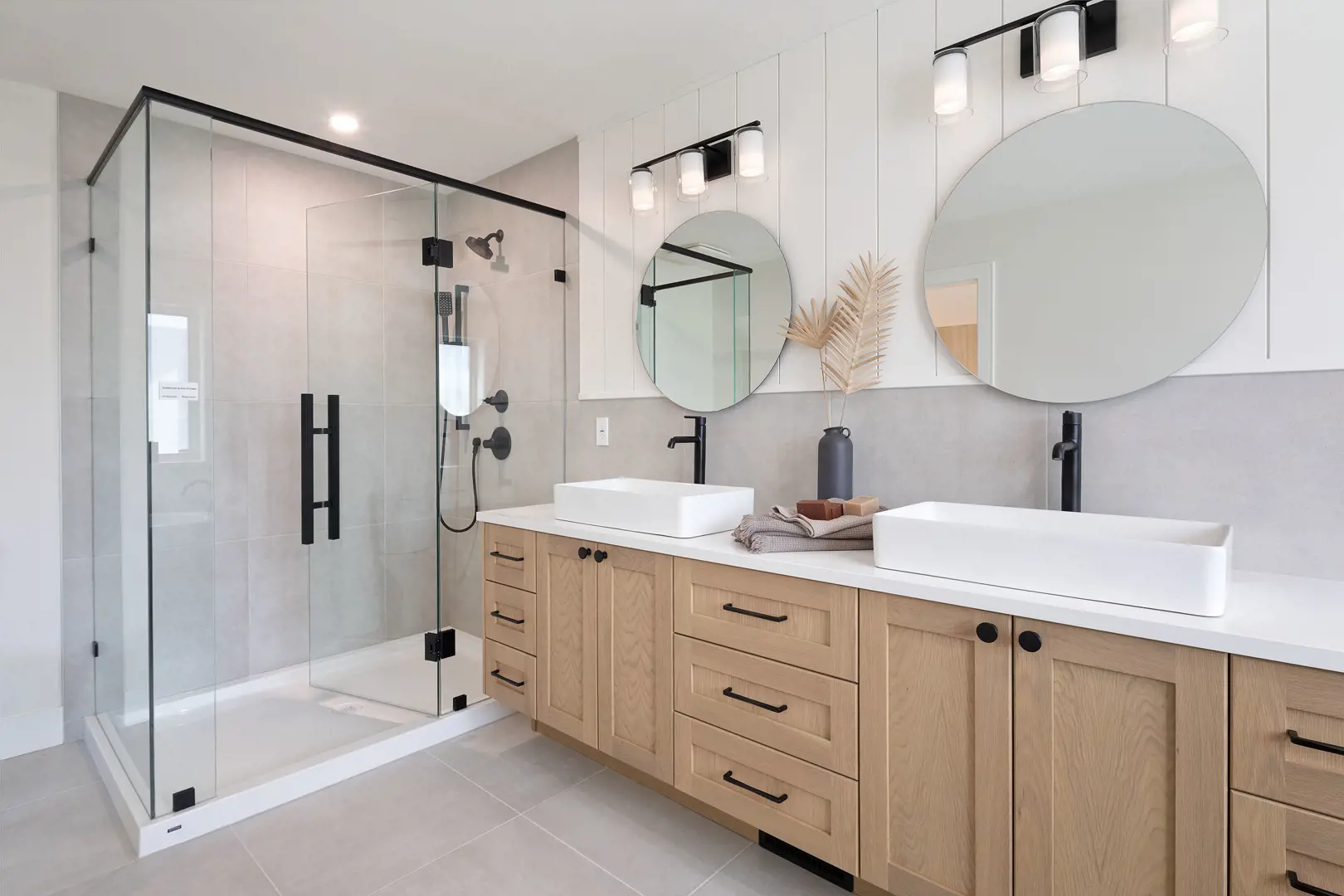 Ridgemont – Primary bathroom with a glass-enclosed walk-in shower, wood-tone double vanity with two vessel sinks, and two round mirrors.