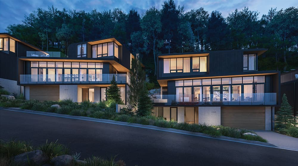 Wildwood at Uplands – Dusk rendering of modern dark-toned homes on a wooded hillside with lit interiors visible through large windows.