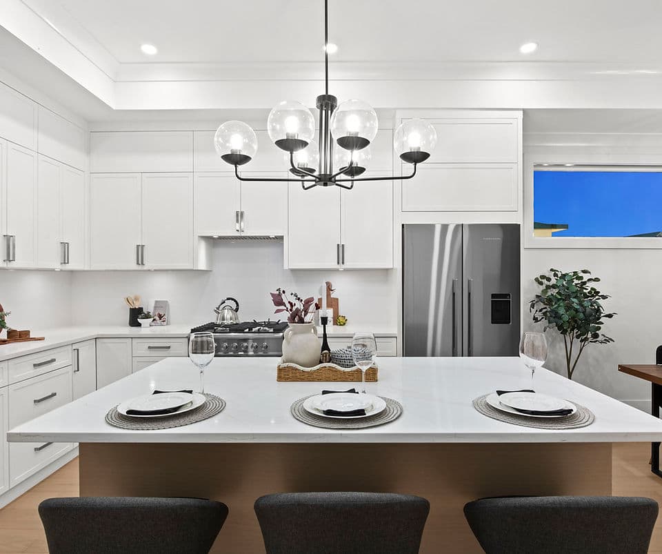 Grandview Walk – A modern open-concept kitchen features a large white marble island set for three, illuminated by a striking black multi-globe chandelier. The space includes crisp white shaker cabinetry, stainless steel appliances, and sleek barstool seating against a warm wooden base.
