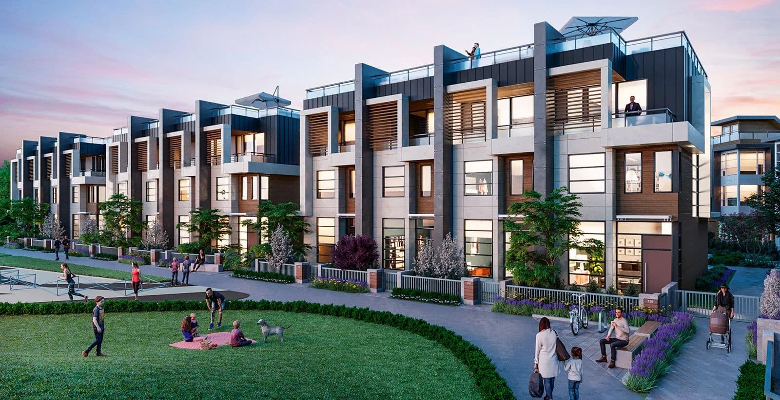 Belle Isle North – A row of modern three-story townhomes with dark metal paneling, wood accents, and private rooftop patios sits behind a paved pedestrian pathway and green lawn. People and pets enjoy the outdoor community park area during dusk, bathed in warm sunset lighting.