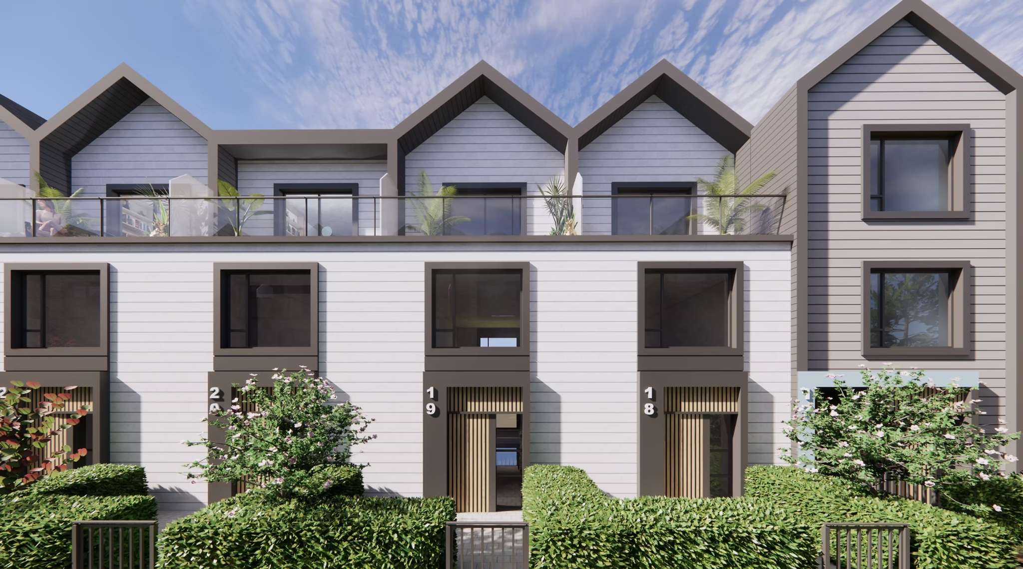 8899 Spires – A modern row of townhomes featuring light grey horizontally slatted siding, dark framed windows, and pitched rooflines under a clear daytime sky. Private ground-level entrances are framed by manicured green hedges, while an upper-level balcony with a glass railing sits above.