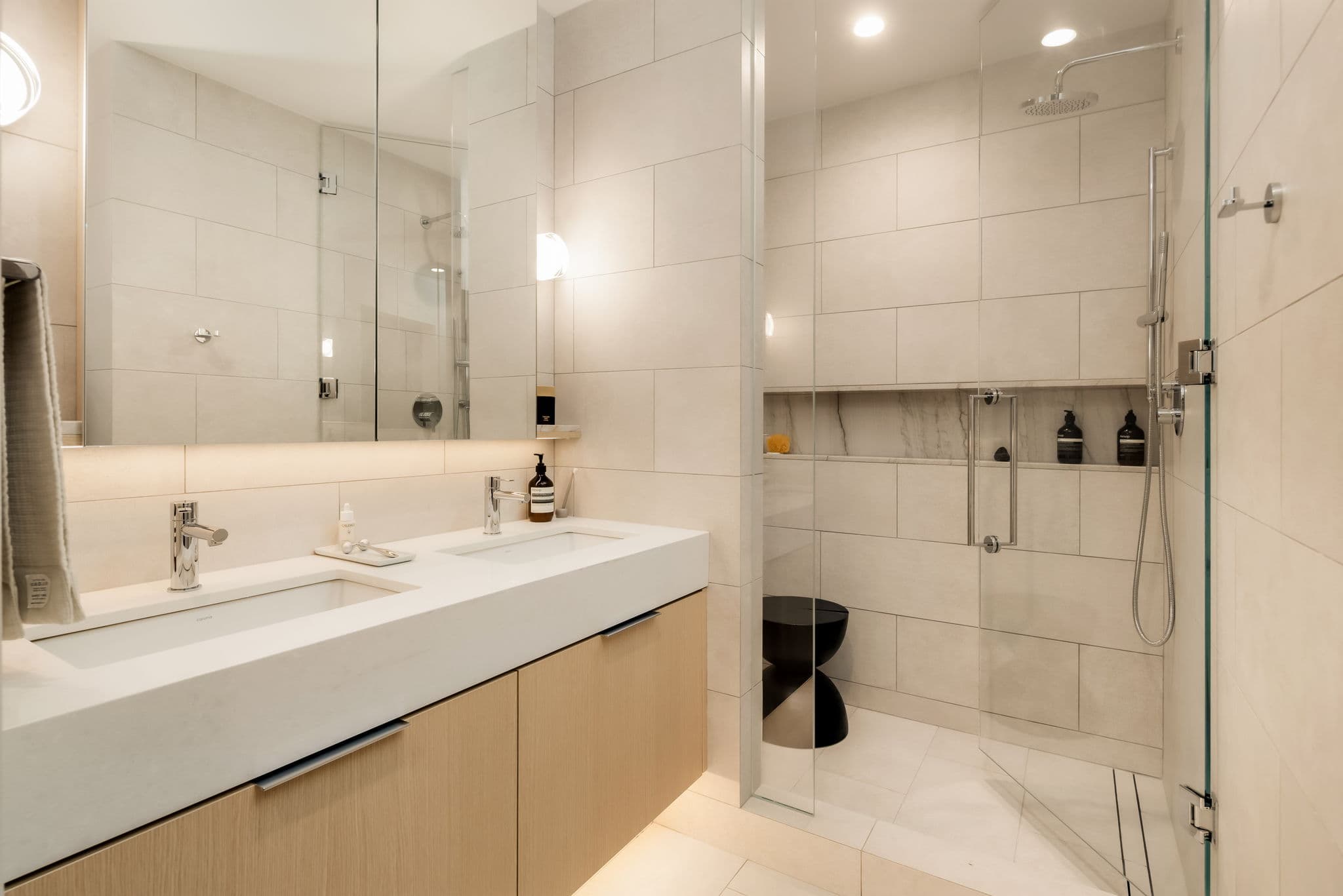 Ashleigh Oakridge Condos – Bathroom photo with a long double vanity and a large tiled walk-in shower with rain shower head and marble niche.