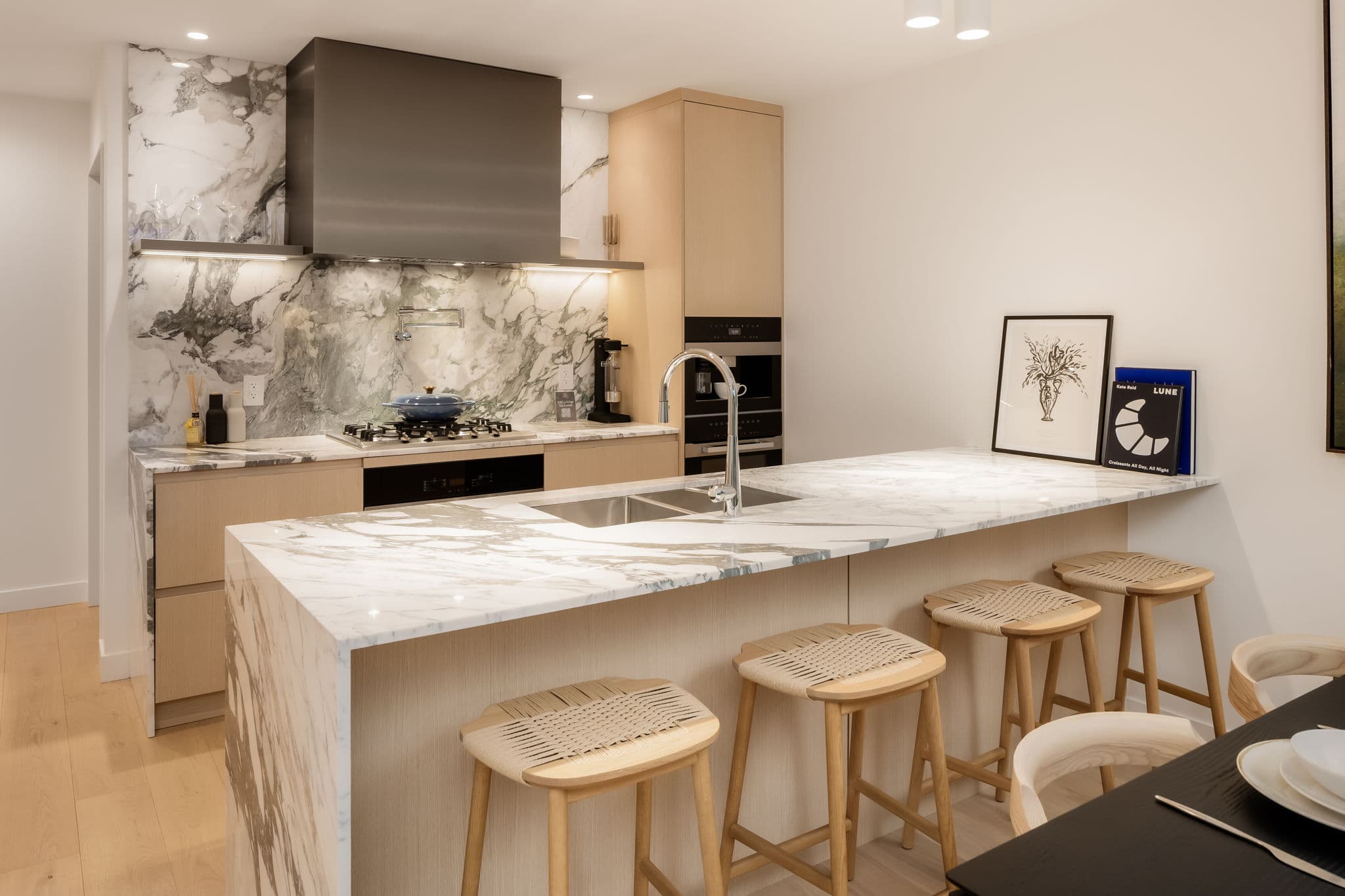 Ashleigh Oakridge Condos – Show-suite kitchen photo with a dramatic marble waterfall island, wood cabinetry, and woven bar stools.