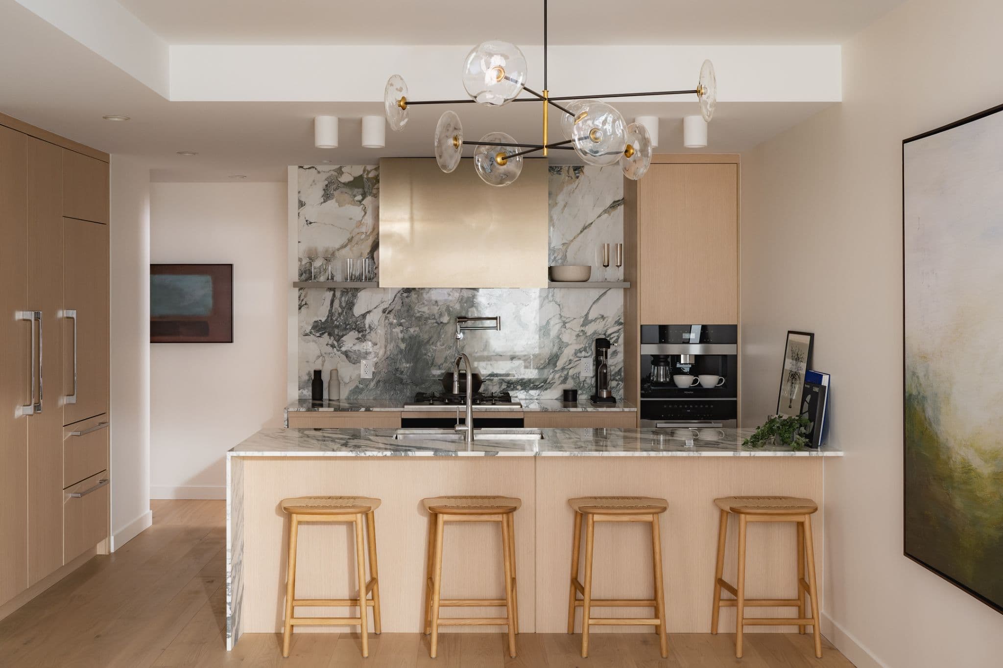 Ashleigh Oakridge Condos – Show-suite kitchen photo with green-veined marble backsplash, brass range hood, and a modern glass-orb chandelier.