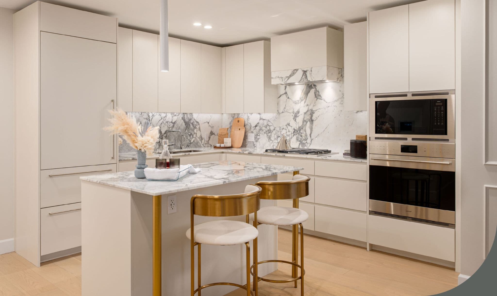 Raphael – Kitchen with cream cabinetry, marble backsplash and range hood, built-in Wolf oven and microwave, and an island with gold-legged bar stools.