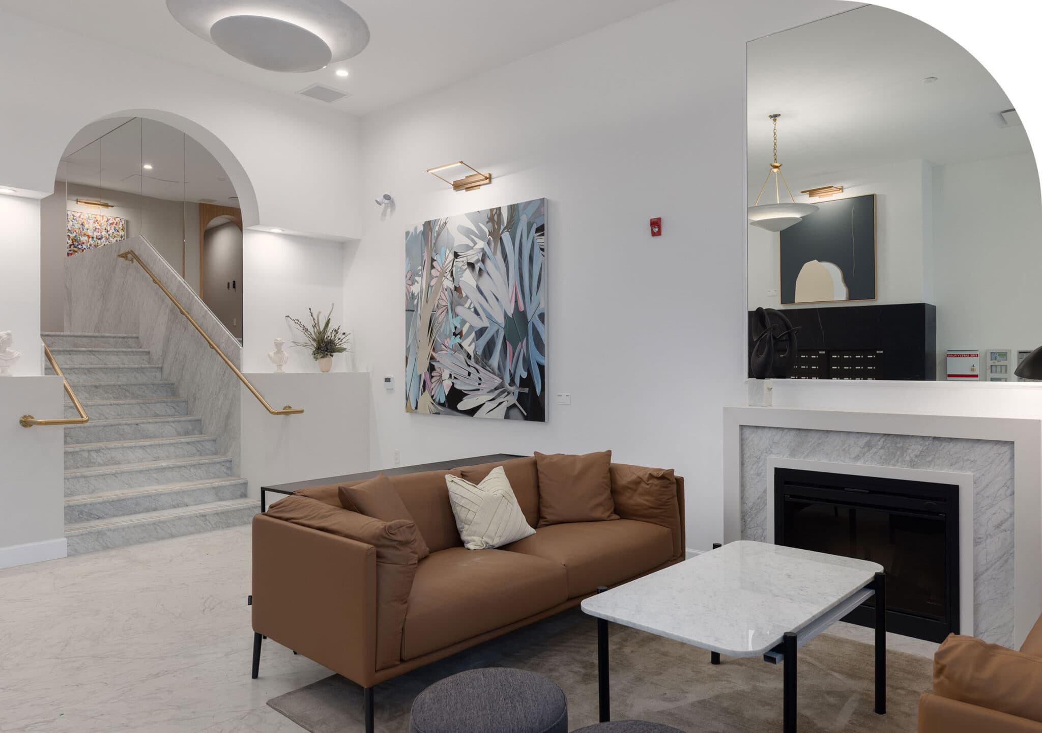 Raphael – Building lobby lounge with a marble staircase, a tan leather sofa, artwork, and a fireplace near the mailroom area.