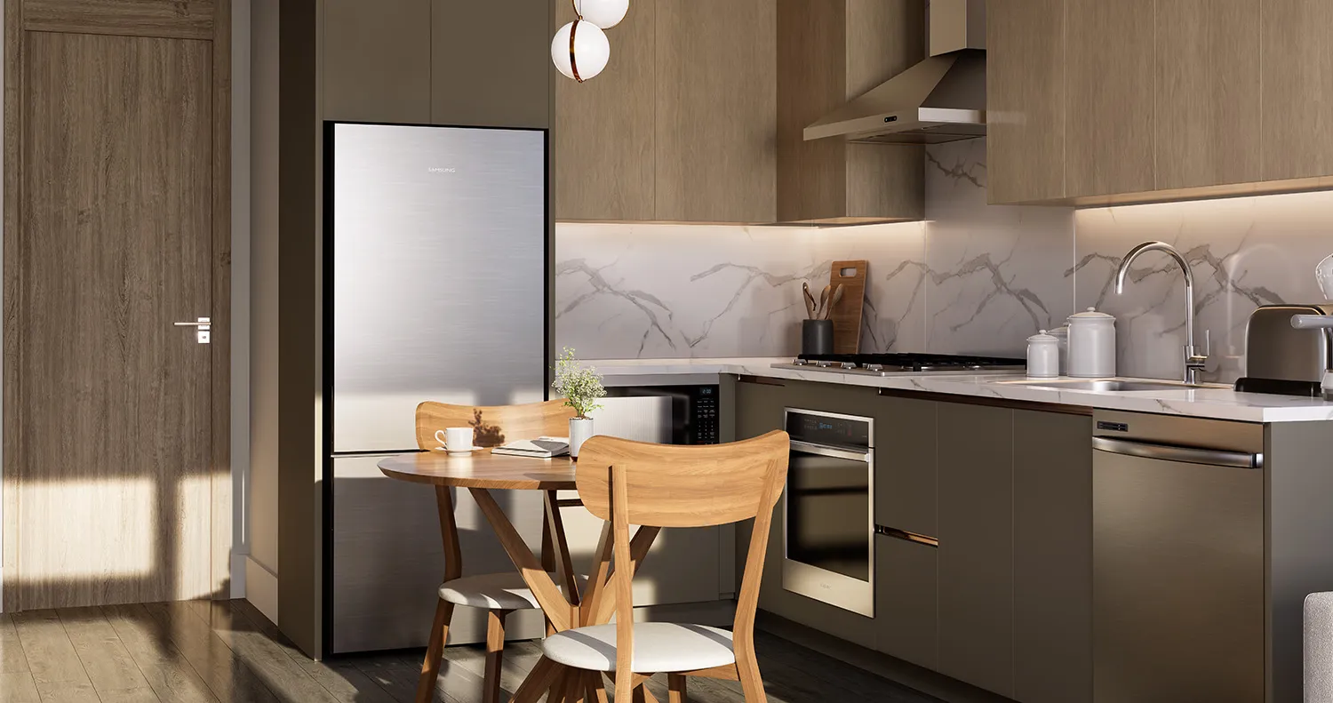 SkyLiving – A kitchen nook with a small round wood table and two chairs beside a stainless steel fridge, with an oven and cooktop along the counter.