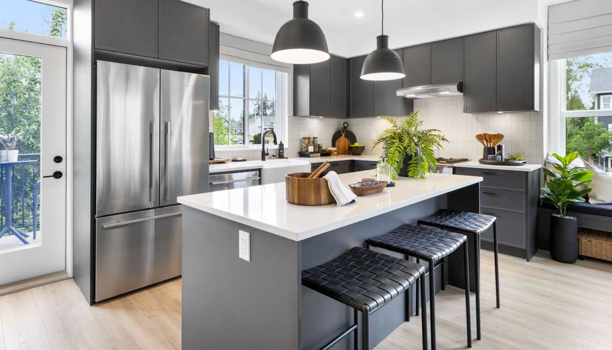 Heath West – Kitchen with dark gray cabinets, stainless steel fridge and range, an island, and a glass door leading to a small balcony.