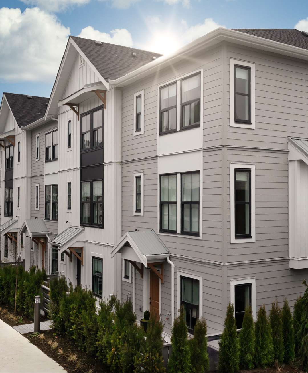 Heath West – Row of three-storey gray and white townhomes with black-framed windows, seen from the street with landscaped hedges in front.