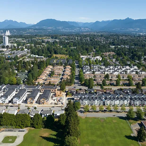 Fleetwood Village 2 – Aerial drone view over the suburban neighborhood under construction, with rows of townhomes, a sports field, and mountains on the horizon.