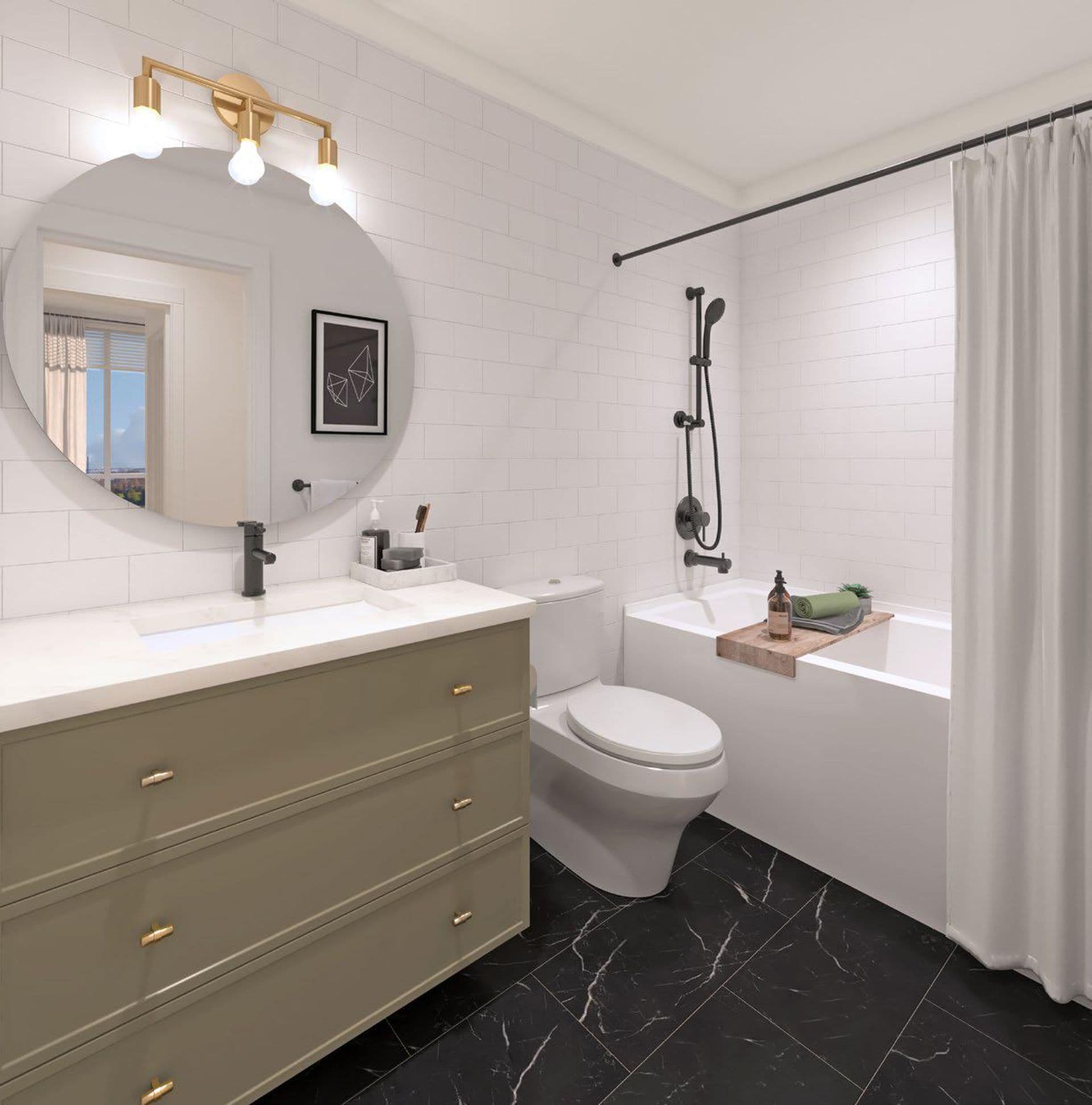 Bastille – Bathroom with white subway tile, a round mirror with a brass vanity light, olive-green vanity with brass hardware, a toilet, and a tub/shower with a shower curtain.