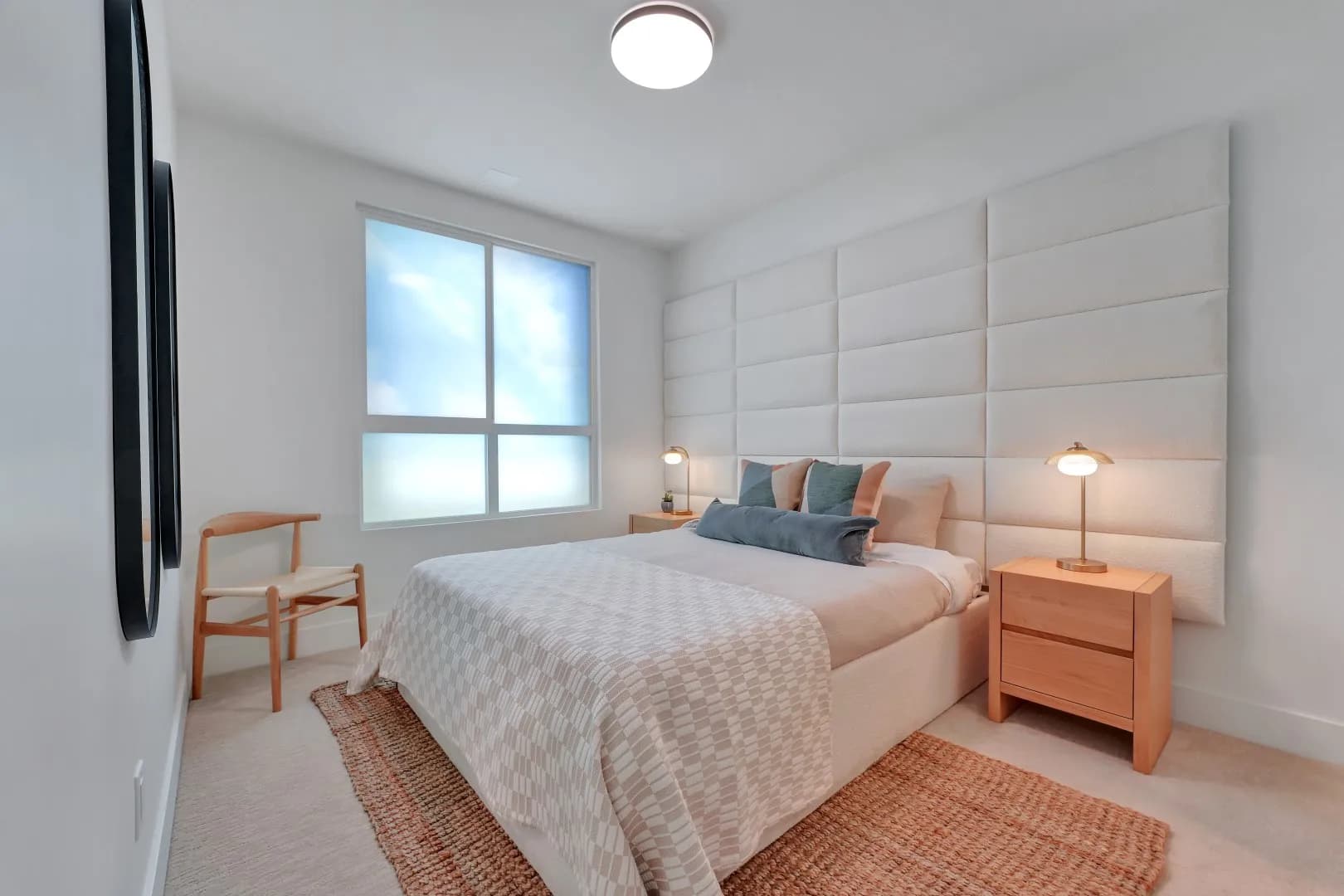 Jethro – Wide view of the same upholstered-wall primary bedroom with a wishbone-style accent chair and jute area rug.