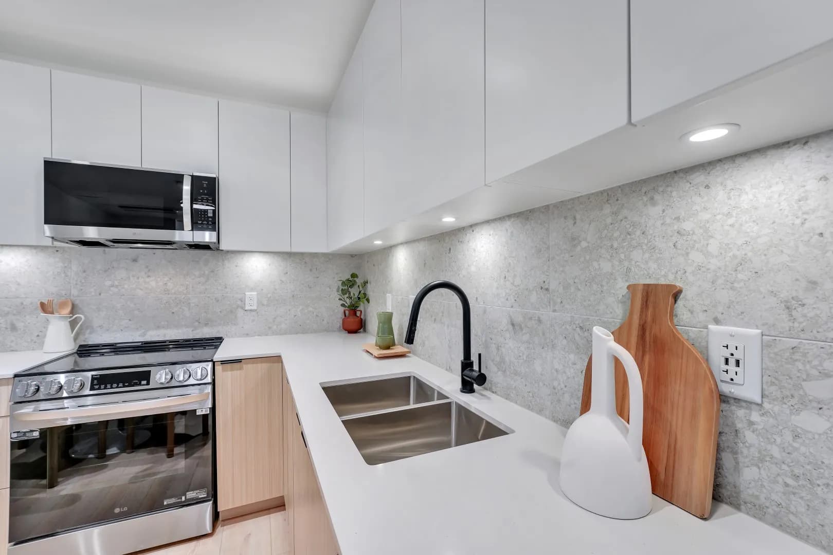 Jethro – Kitchen with white upper cabinets, light wood lower cabinets, stone slab backsplash, black faucet, and stainless range and microwave.