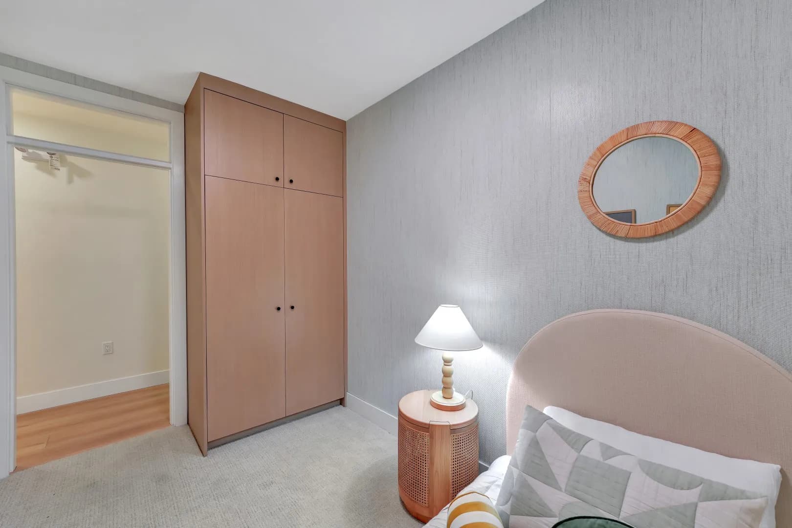 Jethro – Wider view of the same children's bedroom showing a wood wardrobe closet, oval rattan-framed mirror, and doorway to another closet.