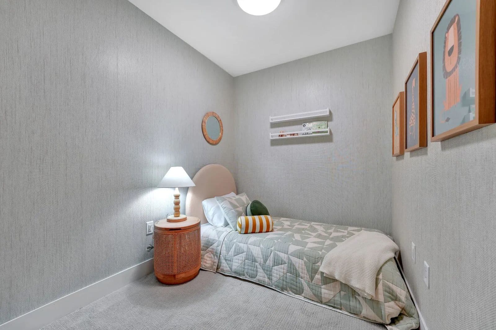 Jethro – Small children's bedroom with a pink upholstered headboard on a twin bed, round mirror, wall-mounted bookshelf, and framed animal artwork.