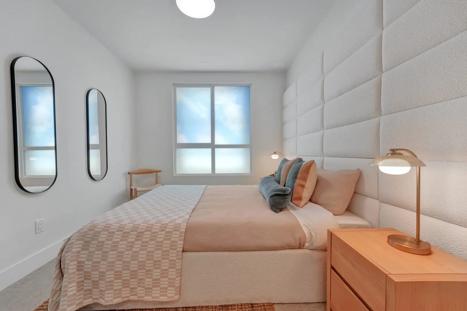 Jethro – Primary bedroom with a tall upholstered boucle headboard wall, wood nightstands, and modern table lamps.