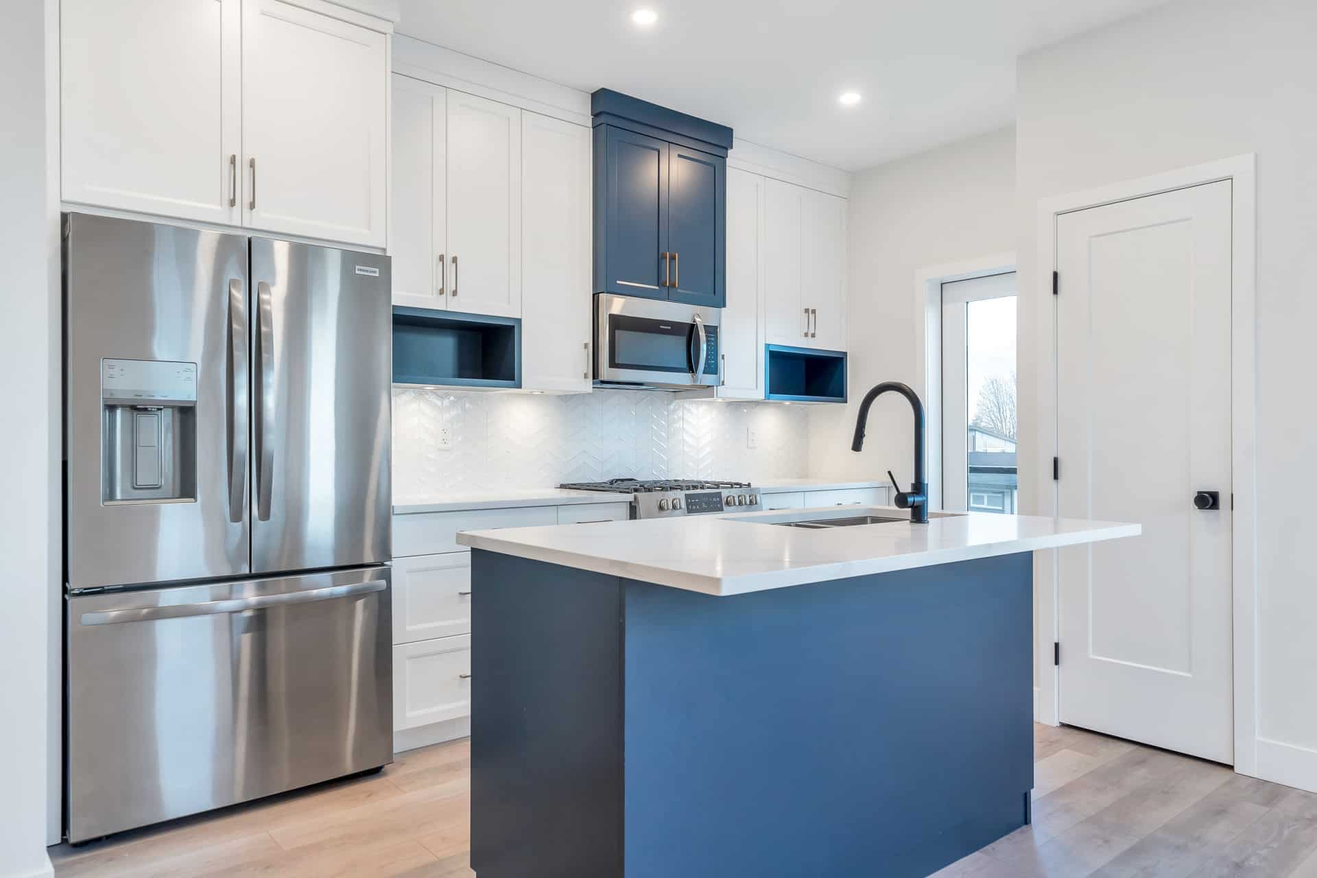 Osprey Ridge – Kitchen with white and navy blue cabinetry, stainless-steel fridge, gas range, and an island with a white countertop.